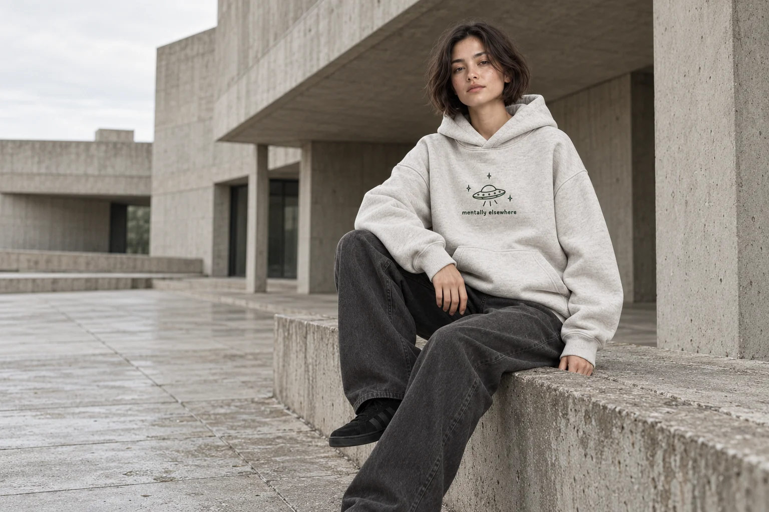 The Mentally Elsewhere hoodie worn during a quiet break outside a concrete building
