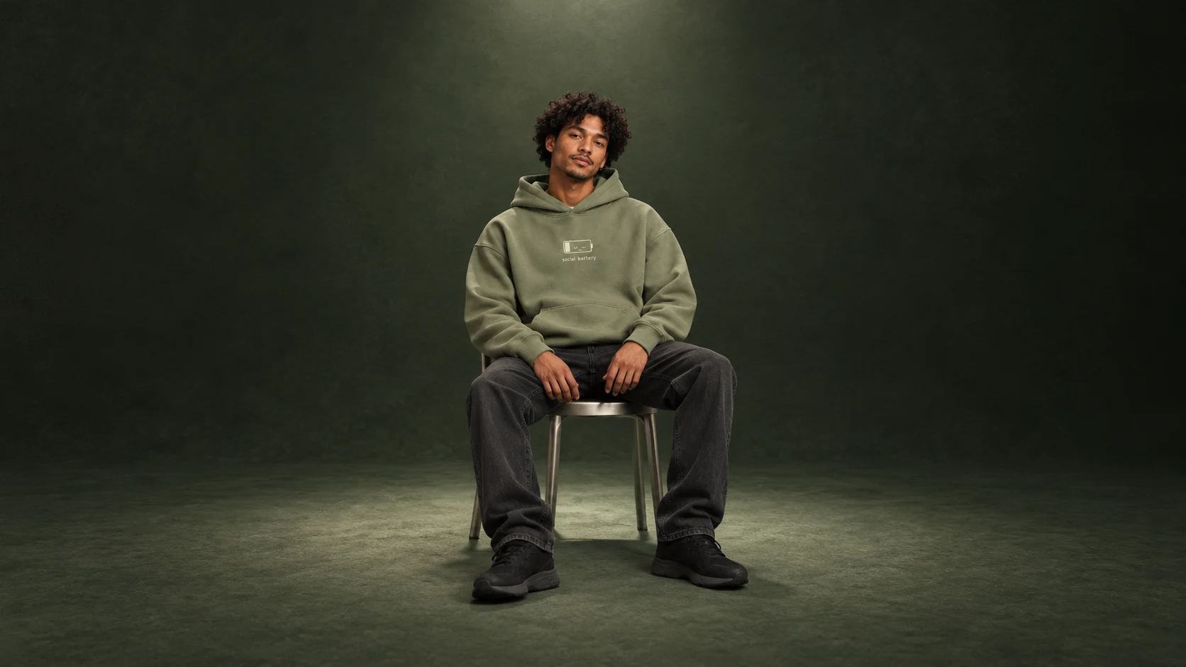 Social Battery hoodie campaign: a model taking a quiet moment in a forest-green studio